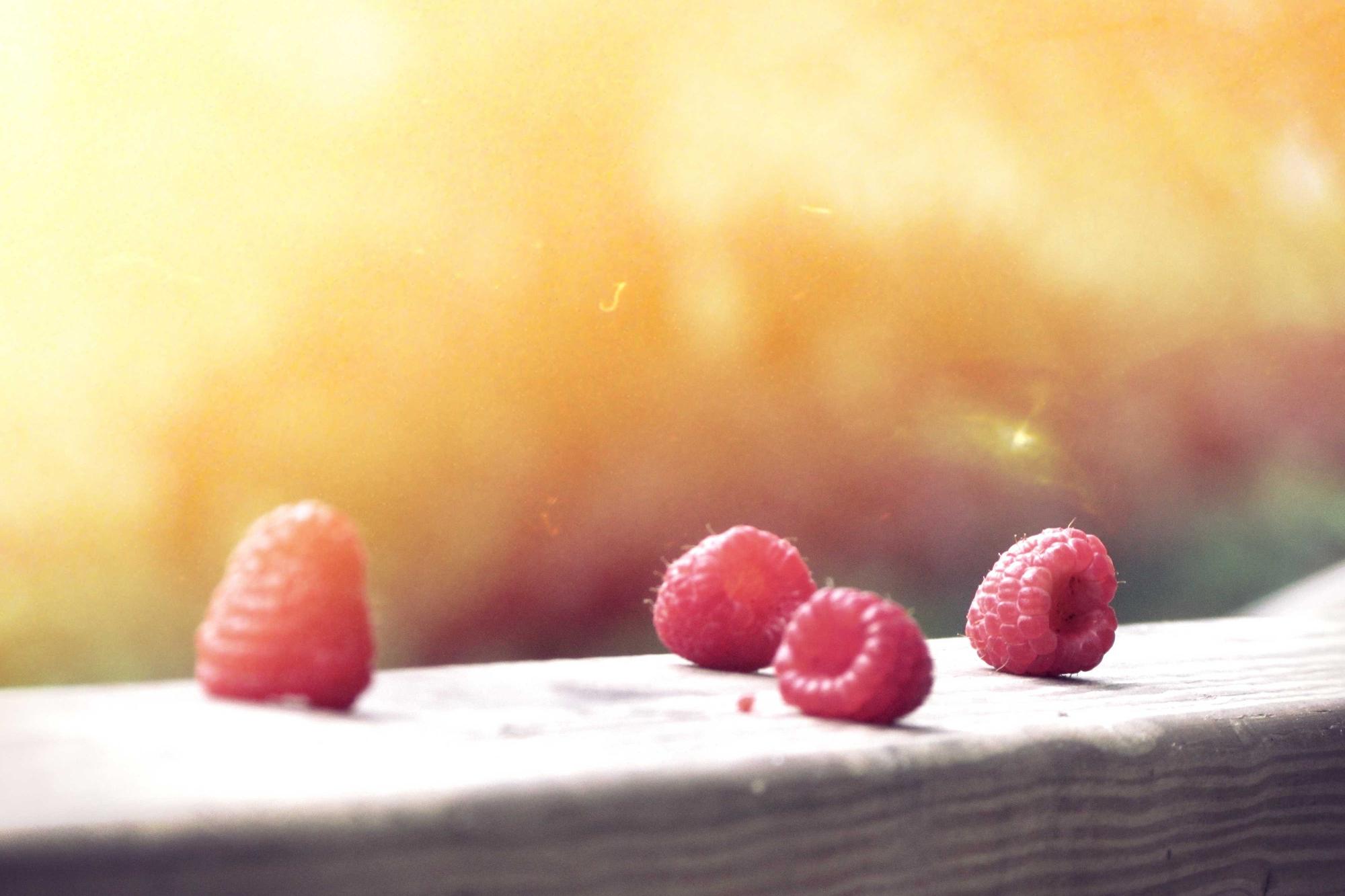 Three raspberries on a pale ledge in warm light