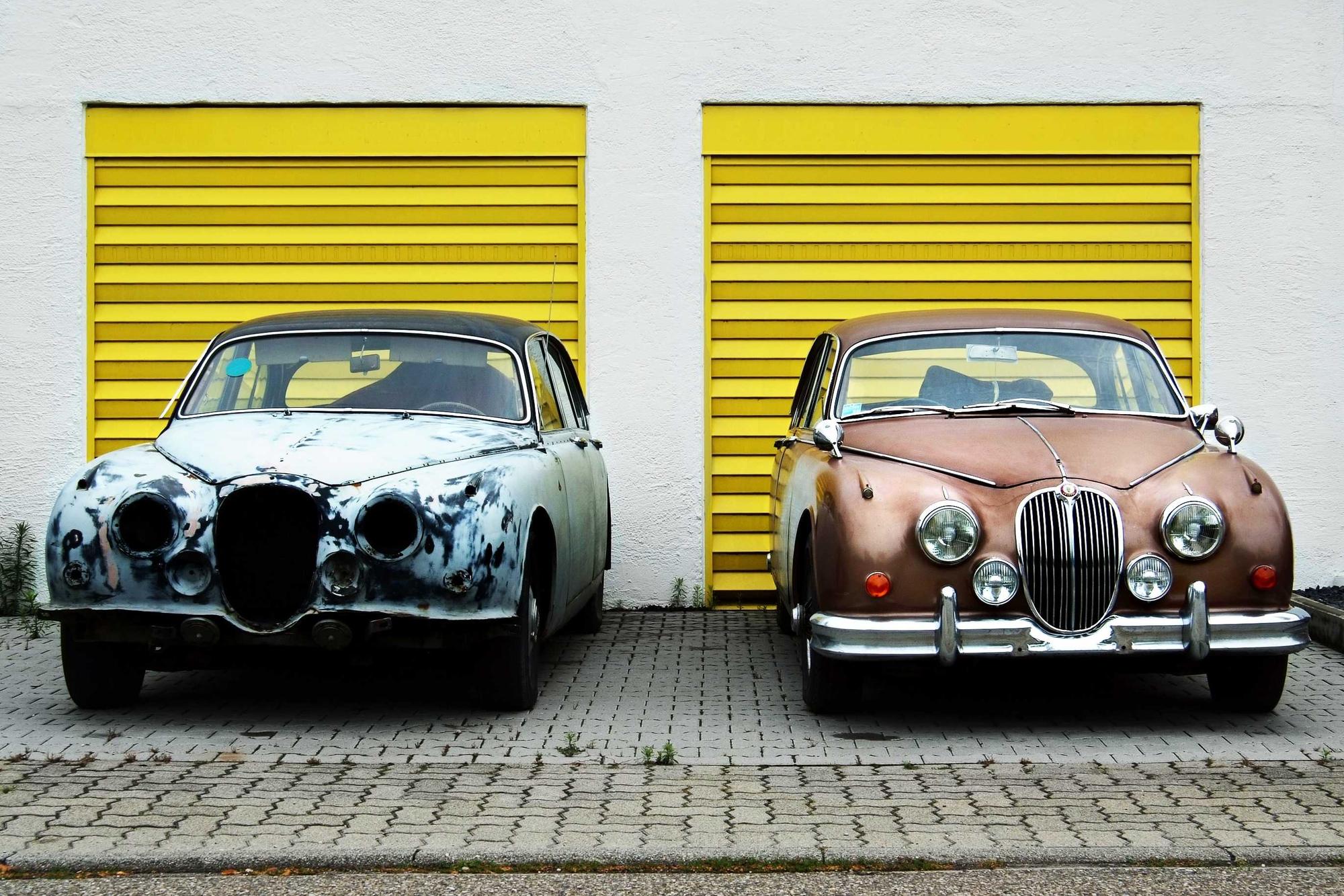 Two vintage cars parked in front of bright yellow garage doors