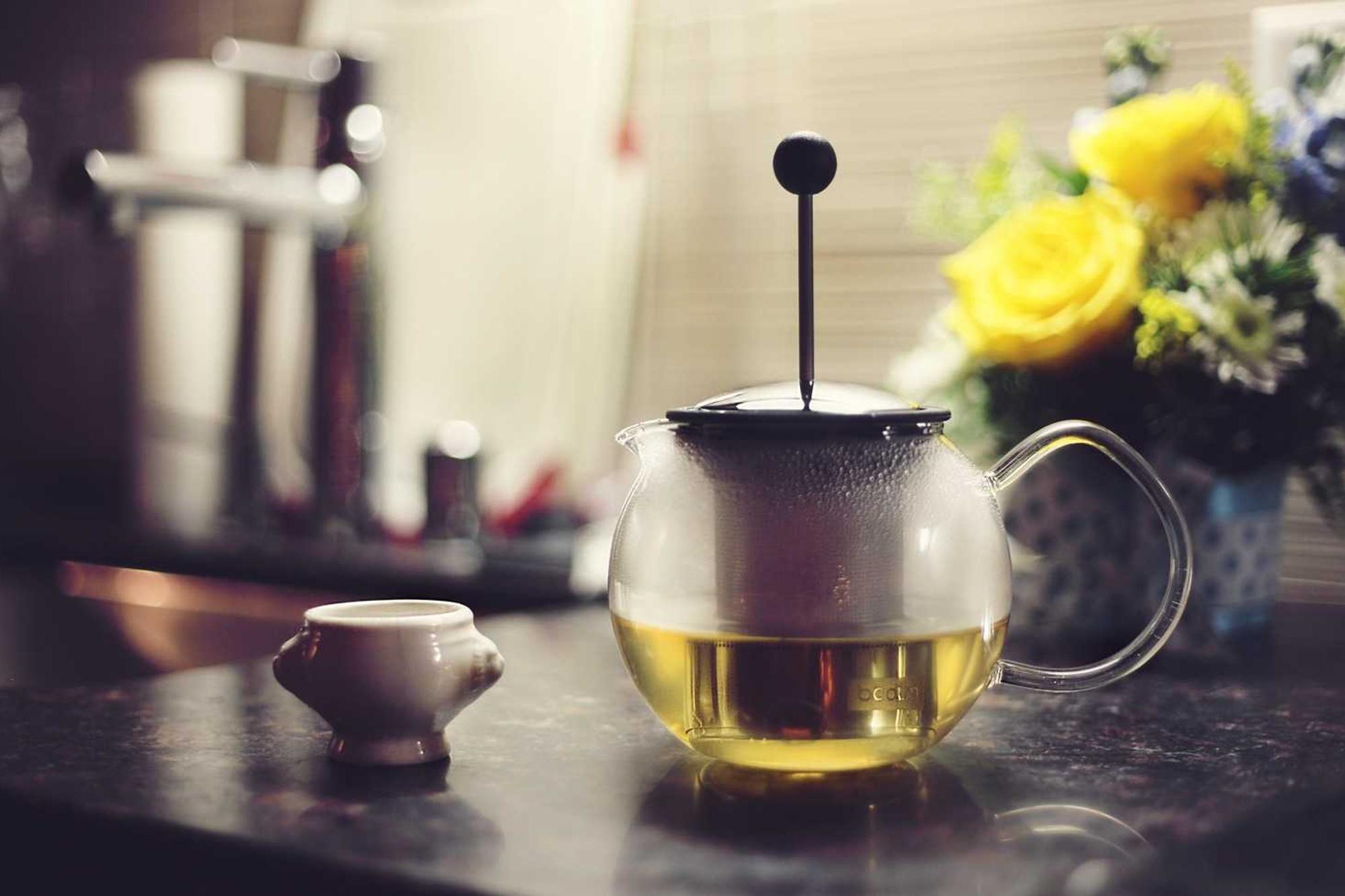 A glass teapot beside a small bunch of yellow roses