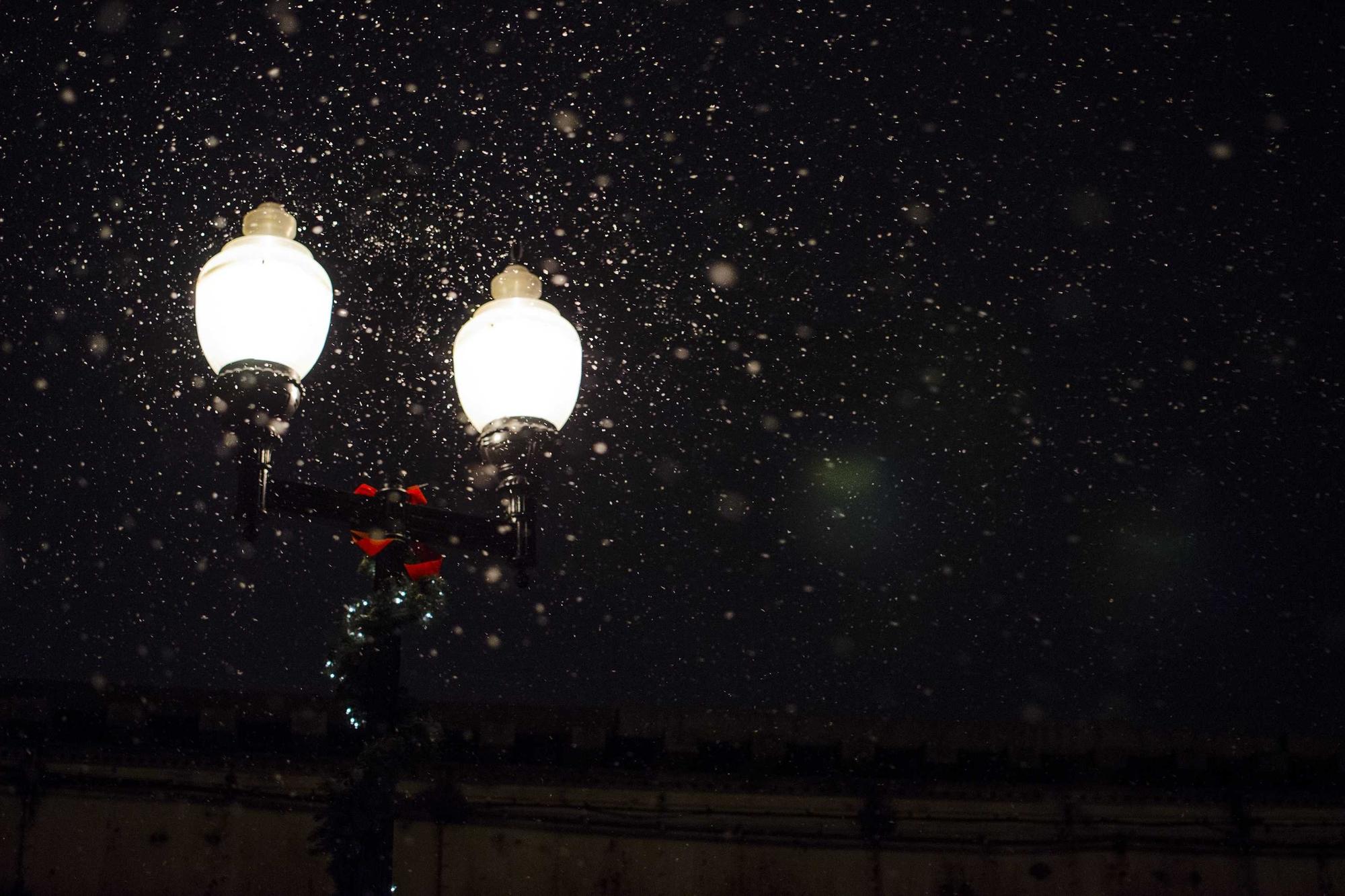 Two street lamps glowing at night while snow falls