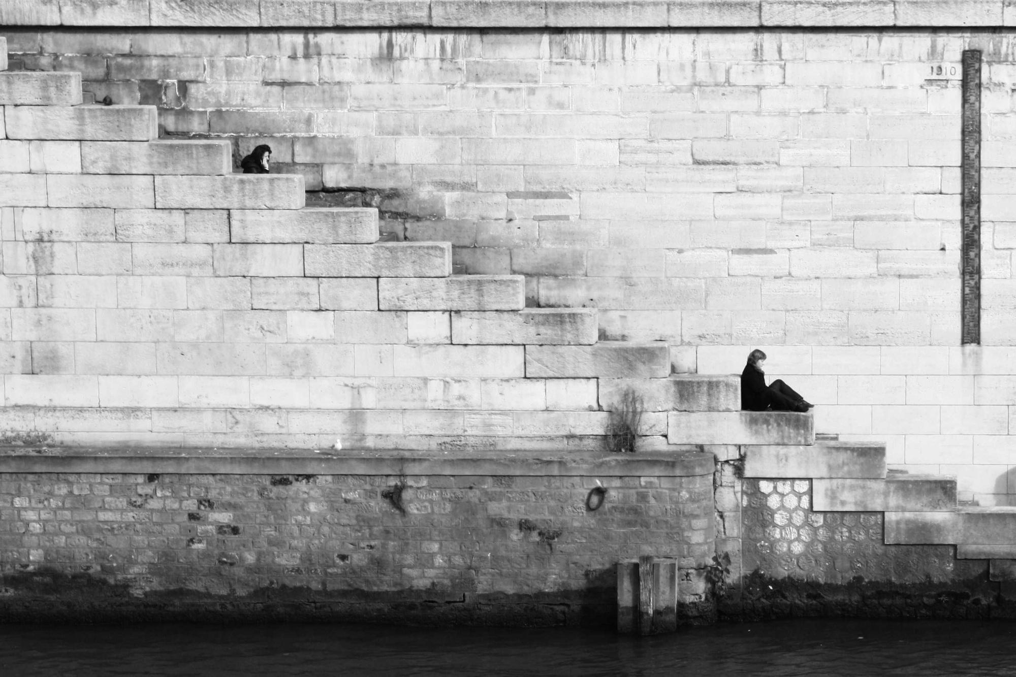 A person sitting alone on stone steps beside the water