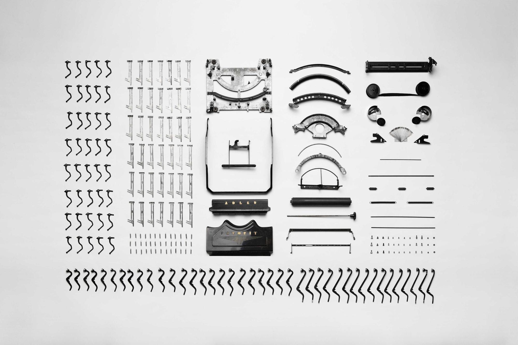 Typewriter parts laid out in rows on a white surface